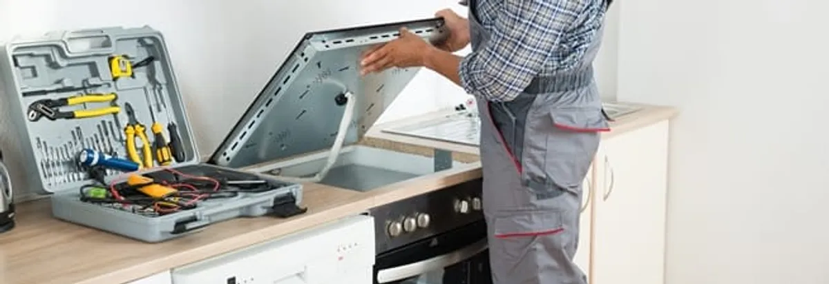 Cooktop repair technician lifting a built-in stovetop for service in Allentown, PA