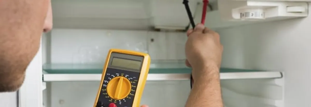 Refrigerator repair technician testing electrical components with a multimeter in Allentown, PA